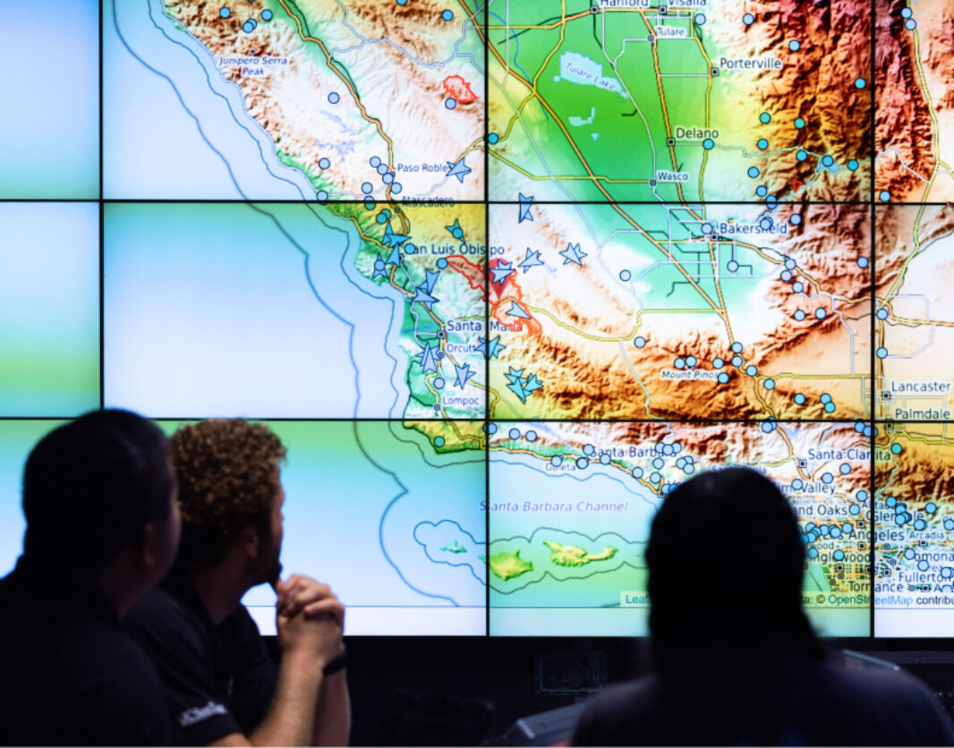 Three people are reviewing a map of California on a large array of screens pooled together to show a single image
