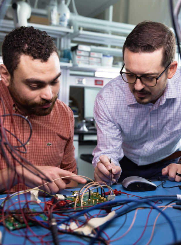 Two men are working with an electronics panel on a workbench